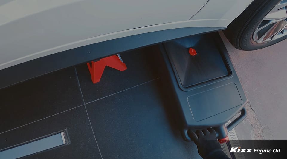 A mechanic placing a drain pan under the car