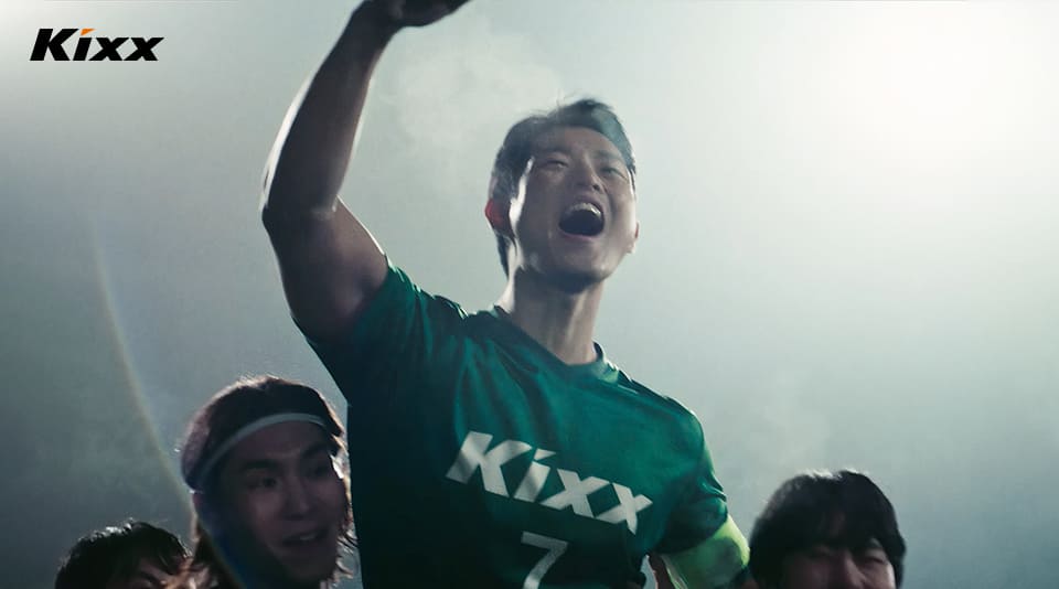 The man raises a fist and cheers against a background of bright stadium lights as silhouetted team members do the same.