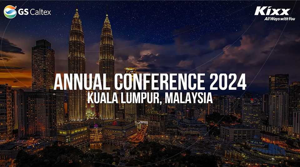 The image promotes the GS Caltex Annual Conference 2024 to be held in Kuala Lumpur, Malaysia. The backdrop features the iconic Petronas Twin Towers, showcasing the city’s skyline at night