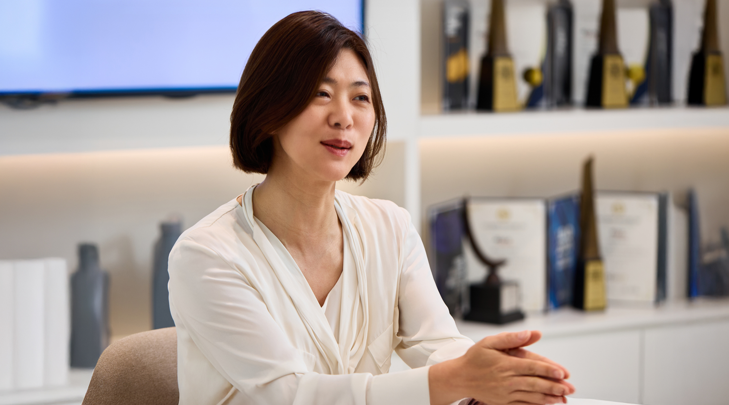 Interviewee Image_4 | Kixx Newsroom Team Leader Ji Seon Park with trophies in the background