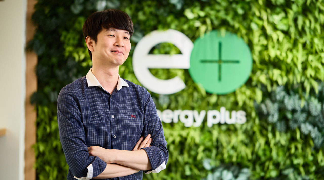Image 5 | Kixx Newsroom Kwan Hee Choi smiles as he crosses his arms in front of a leafy wall.